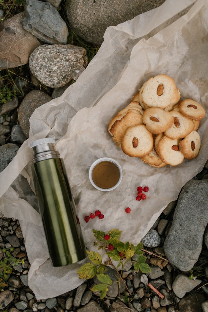 A cozy outdoor picnic scene featuring almond cookies, a thermos, and a cup of tea on parchment paper.